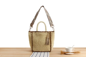 Detail of woven paper straw tote with geometric jacquard strap and fringe tassel charm
