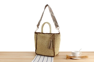 Detail of woven straw tote bag with brown trim, boho shoulder strap and tassel charm