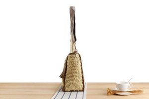 Close-up of handwoven beige paper straw tote bag with folk-pattern strap and leather fringe