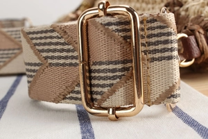 Detail of woven shoulder strap with geometric pattern and gold metal buckle on a straw bag