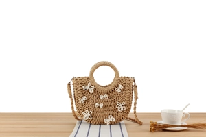 Dettaglio della borsa in paglia intrecciata con fiocchi di perle su legno chiaro