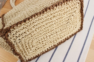 Detail of hand-woven paper rope beach bag showing beige texture and dark brown reinforced base