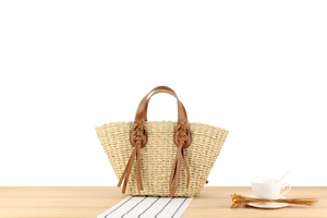 Detail of straw handbag featuring brown leather handles and decorative leather tassels