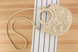 Dettaglio della borsa in paglia beige con fiocchi di perle bianche e manico rotondo
