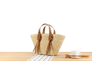 Close-up of woven straw tote bag with brown leather handles and decorative long tassels