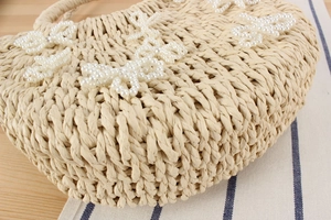 Dettaglio della borsa da spiaggia in paglia intrecciata con farfalle di perle bianche