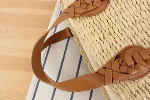 Detail of woven straw tote bag featuring brown braided handles and beige fabric lining