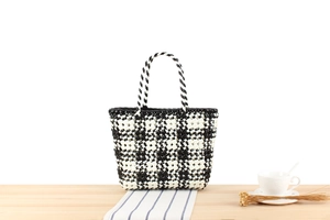 Detailed view of handcrafted black and white checkered PVC woven tote bag on a table