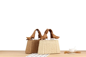 Detail of woven straw handbag featuring a chic leather bow handle on a rustic wooden table
