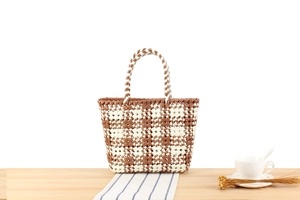 Close-up of hand-woven PVC brown and white checkered tote bag on a wooden table