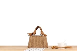 Detailed close-up of woven straw handbag with brown knotted PU leather handles and metal rings