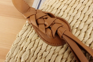 Detail of hand-woven straw bag featuring intricate brown leather braided handle and texture