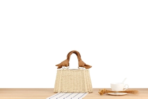 Detail of straw woven bag with brown knotted leather handle on a wooden table with coffee