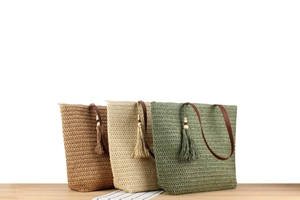 Detailed shot of three woven straw tote bags with leather handles and decorative tassels