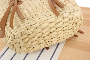 Close-up of a handwoven straw bag featuring intricate textures and brown leather handles