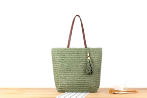 Detail of light green straw tote bag with brown leather handles and fringe tassel charm