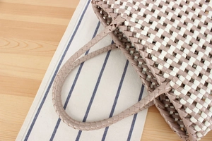 Détail d'un sac cabas tissé à la main en PVC avec motif à carreaux gris et anses robustes