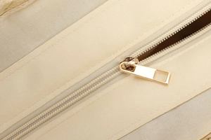 Detailed macro view of the gold metal zipper and smooth beige woven lining of the bag