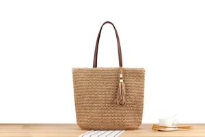 Detail showing a large straw tote bag with brown leather handles and wood bead tassels