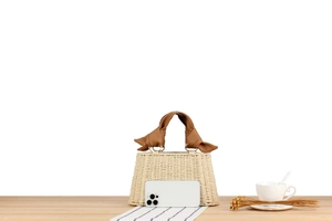 Detail of white straw woven tote with oversized brown leather knot handles on a table