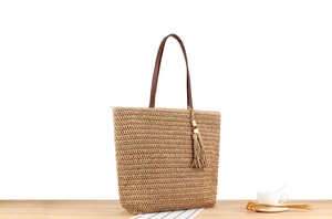Detail of straw tote bag with brown leather handles and decorative tassel ornament
