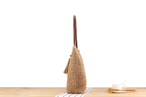 Close-up of straw tote bag featuring brown leather straps and side tassel detail