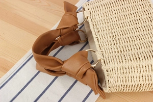 Detail of straw woven tote bag featuring brown leather knotted handles and metal rings