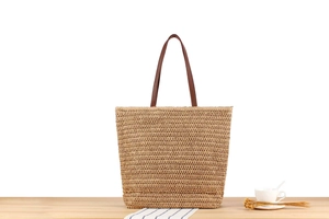 Close-up of a large straw tote bag featuring brown leather handles on a summer table set