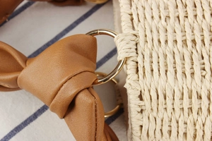 Close-up of beach straw handbag featuring brown leather knotted handle and gold metal ring