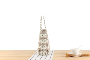 Detail of white and brown checkered woven tote bag placed on a wooden table with decor