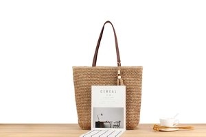 Large straw tote bag detail with dark brown leather handles and wooden bead tassel decor