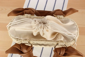 Detail of straw woven bag featuring a brown leather handle with an elegant bow accent