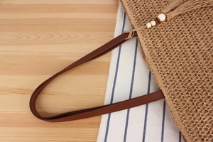 Detail of straw woven tote with brown PU leather handles and beaded tassel charm