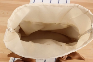 Detailed top view of a white canvas drawstring bag with brown leather knotted handles