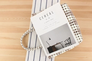 Detail of checkered woven PVC tote bag on wooden table with a minimalist lifestyle setting