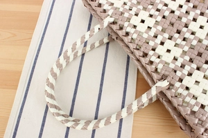 Detail of grey and beige PVC woven handbag texture on a wooden surface closeup