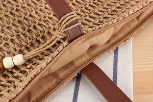 Detail of straw tote bag showing smooth zipper closure and premium brown leather handle