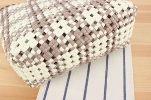 Detailed view of the gray and white woven PVC plastic tote bag on a wooden table