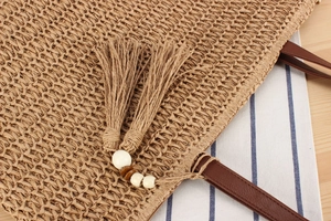 Close-up of woven straw tote bag featuring decorative tassels and wooden beads detail
