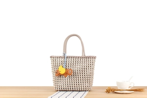 Detail of woven plastic handbag with colorful elephant charm on a wooden table