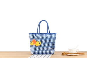 Detail of blue and white woven tote bag with yellow elephant charm on wooden surface