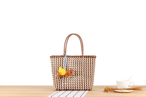 Detail of woven tote bag featuring brown diamond patterns and a leather elephant charm