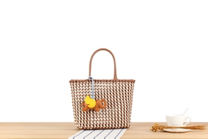 Detail of woven straw tote bag with leather elephant charm on a wooden table