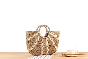 Detail of a large woven straw handbag with striped pattern and round handles on a wood desk