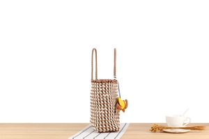 Detail of woven brown and white cylinder bag with leather strap and elephant charm