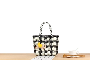 Detail of checkered woven tote bag with elephant charm on wooden table background