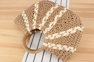 Detail of a semi-circular woven straw handbag with two-tone pattern and round handles