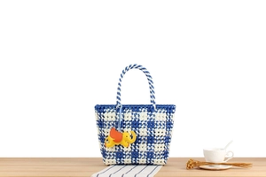 Detail of blue and white checkered woven tote bag with a yellow elephant charm