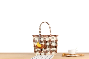 Detail of woven checkerboard tote bag with a decorative brown elephant leather pendant