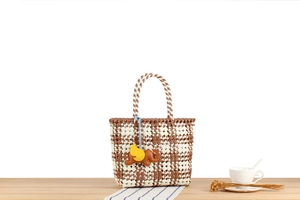 Detail of woven plastic tote with checkered pattern and brown elephant leather charm